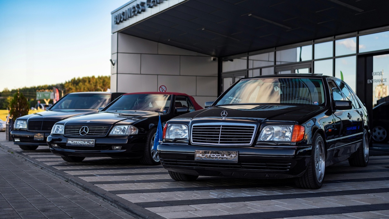 Luxury dealership service area with technicians servicing a premium sedan.