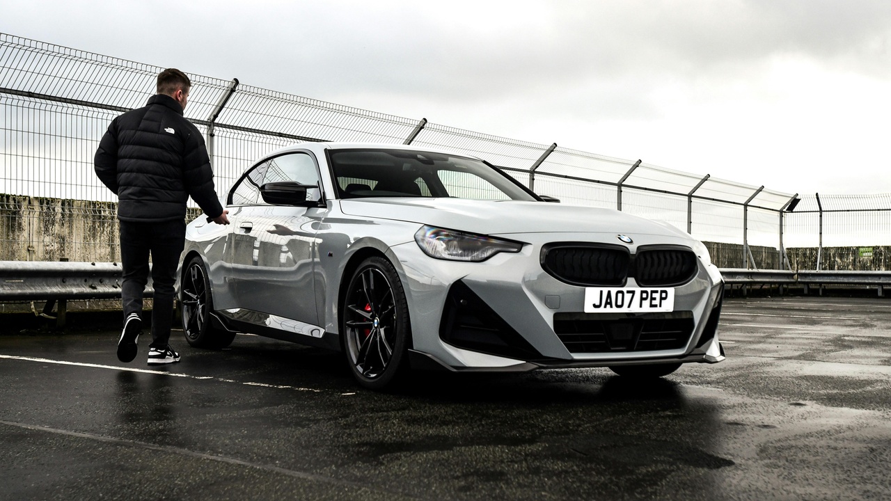 Owner standing beside a coupe on a scenic drive, illustrating lifestyle and ownership appeal.