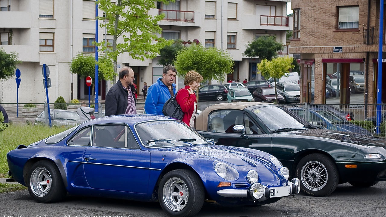 Jaguar E-Type and Ferrari 250 GTO, iconic 1962 sports cars on a coastal road.