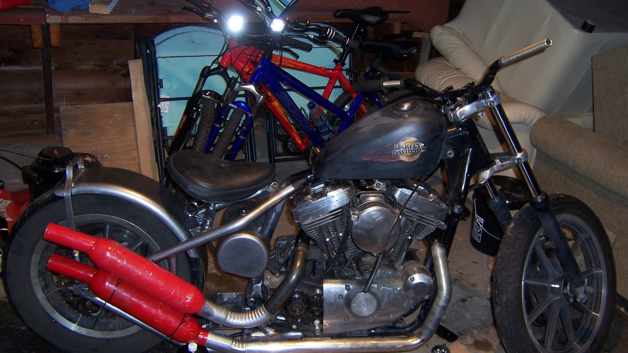 Garage with cafe racer parts laid out: seat cowl, clip-ons, and a vintage tank