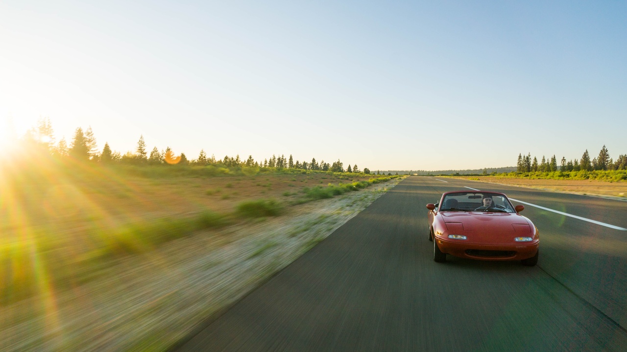 Driver enjoying open-air convertible on scenic coastal road.