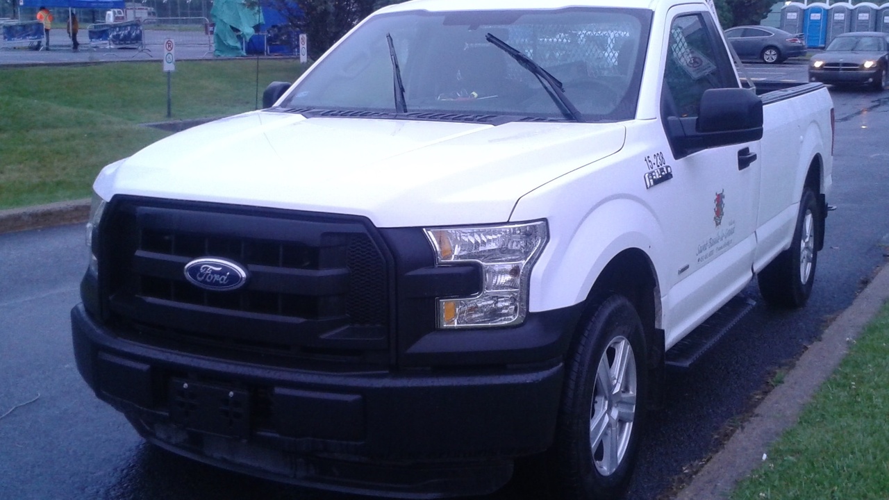 Regular cab pickup parked at a worksite, cost comparison documents on the hood