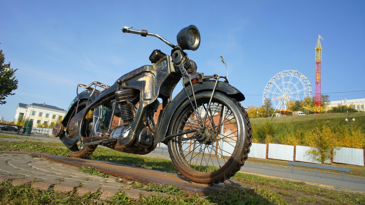 A workshop with a Ural and Dnepr under restoration, parts laid out on benches and a rally photo pinned to the wall