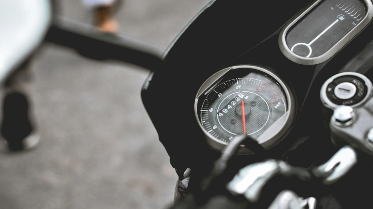 Motorcycle parked at a gas station showing fuel economy and cost considerations on dashboard