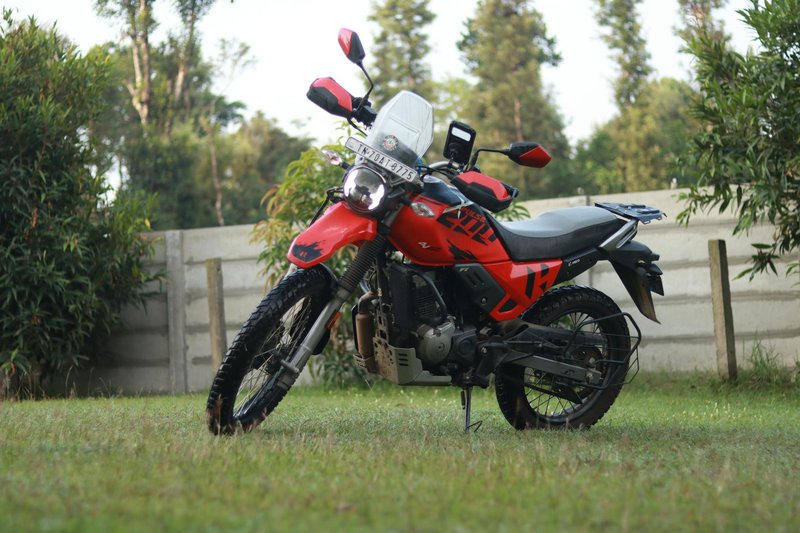 Dual-sport red motorcycle parked on grassy lawn in Madikeri, Karnataka, India.