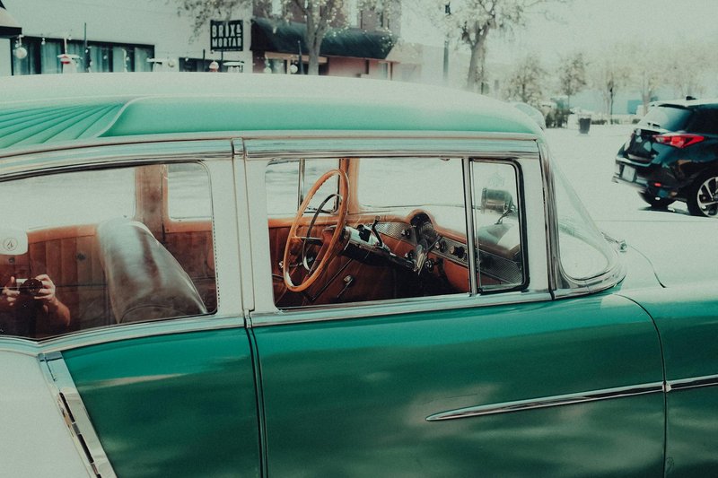 Close-up of a vintage green car interior with wooden steering wheel, parked outdoors.
