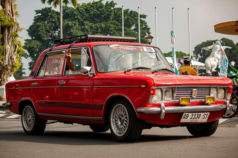 Classic red sedan showcased at an outdoor car event, highlighting vintage automotive style.