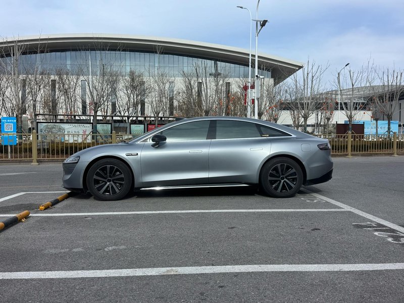 Side view of a sleek silver electric sedan parked in a city lot by a modern building.