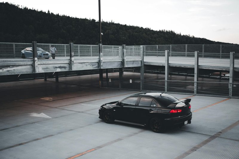 A black car parked alone in a spacious parking lot during twilight, creating a moody atmosphere.