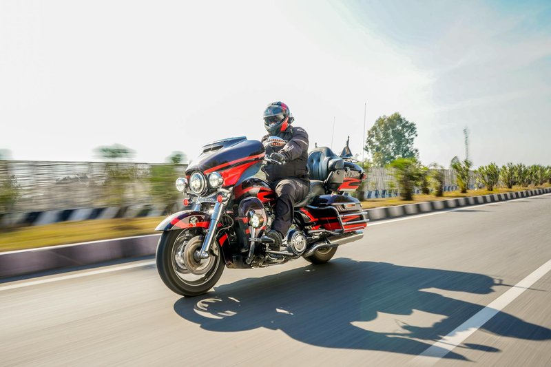 Man on a Harley-Davidson motorcycle riding on an open highway in daylight.