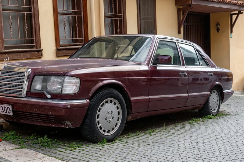 A classic maroon sedan car parked outside on a cobblestone street next to a building.