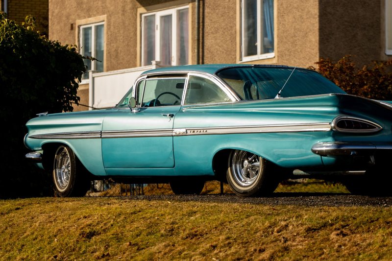 A vintage blue classic car parked in front of a house in Jönköping, Sweden, on a sunny day.