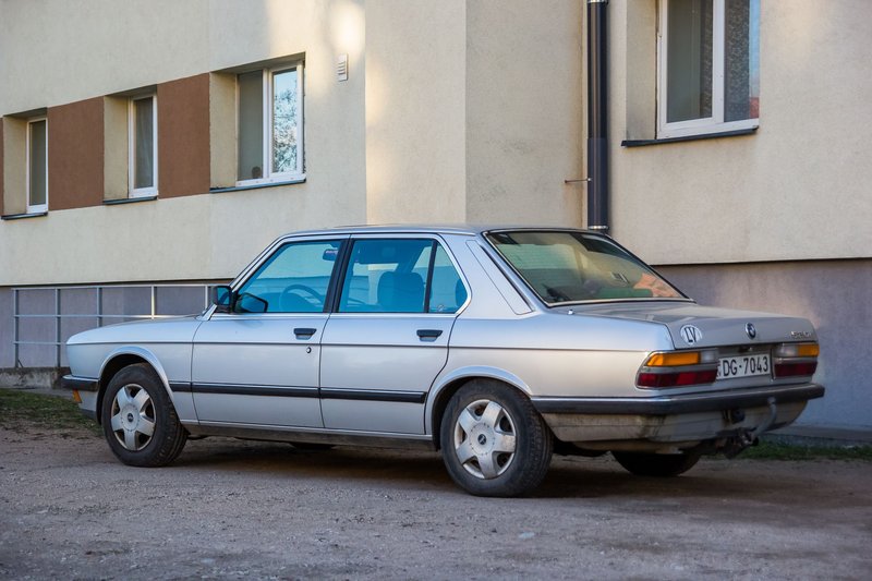 Classic silver sedan parked beside a residential building on a sunny day.