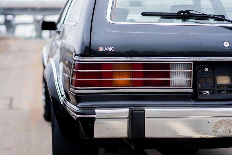 Red and yellow taillights of old fashioned car on gray asphalt road on blurred background