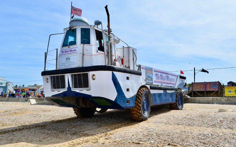 Amphibious vehicle, 'The Wash Monster', on a pebble beach in England under bright skies.