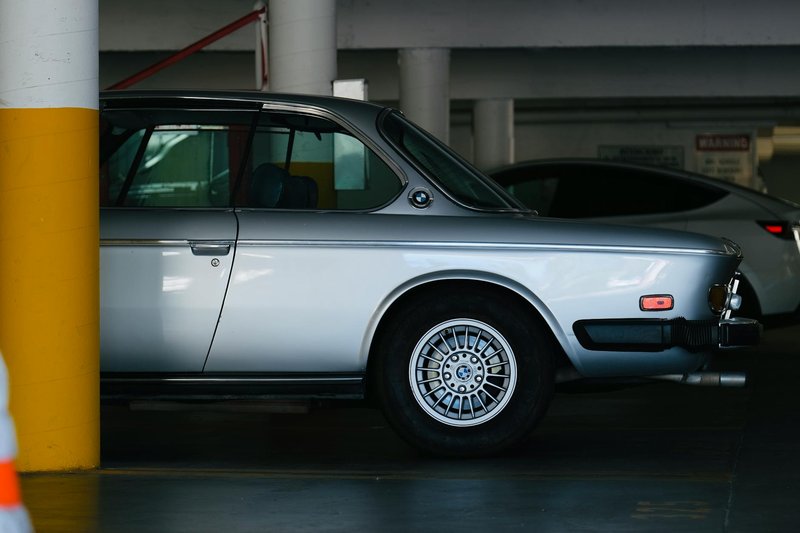 Vintage BMW E9 in a dimly lit urban parking lot with yellow pillars.