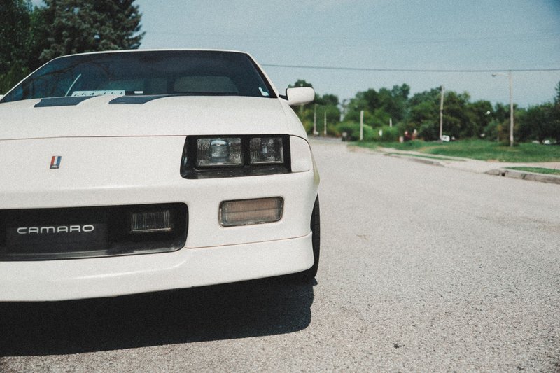 White vintage Chevy Camaro car parked on an empty street during a sunny day.