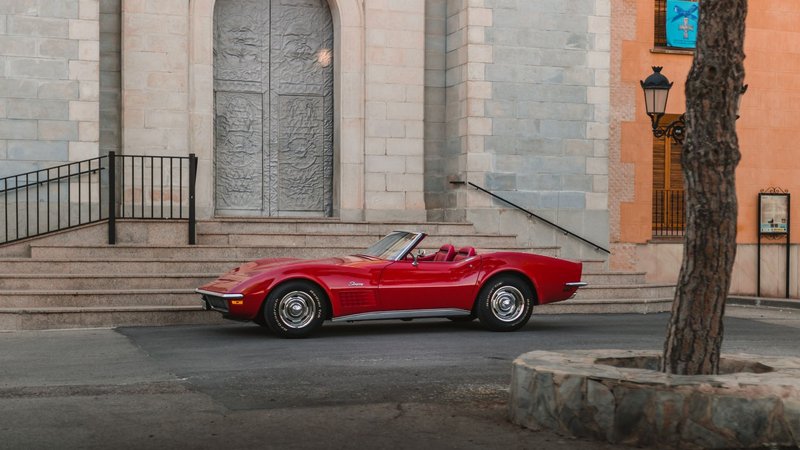 A stylish red vintage Chevrolet Corvette parked on a city street beside a historic building.
