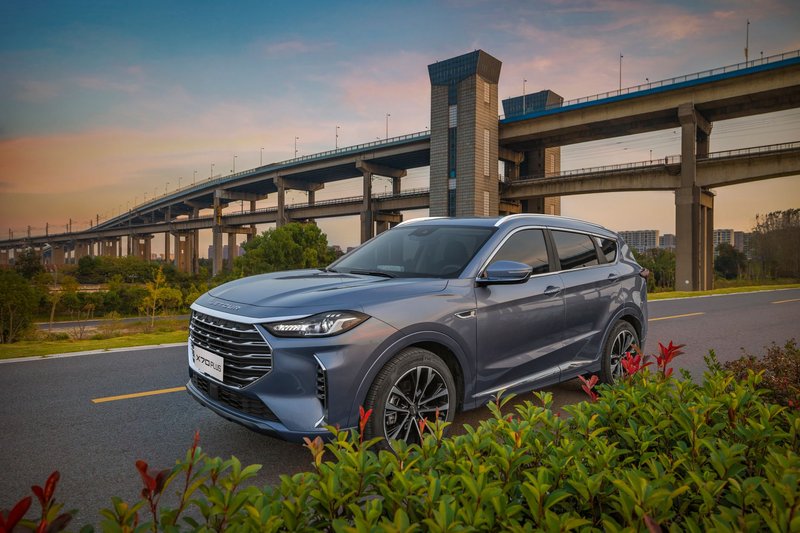 A sleek blue SUV parked on a scenic road with a bridge in the background during sunset.