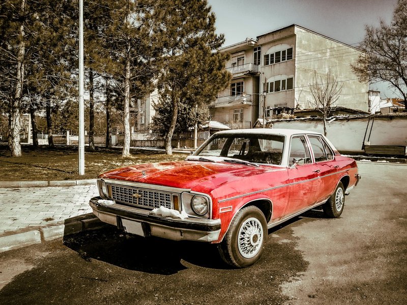 A classic red Chevrolet car parked on a street lined with trees and buildings in Türkiye.