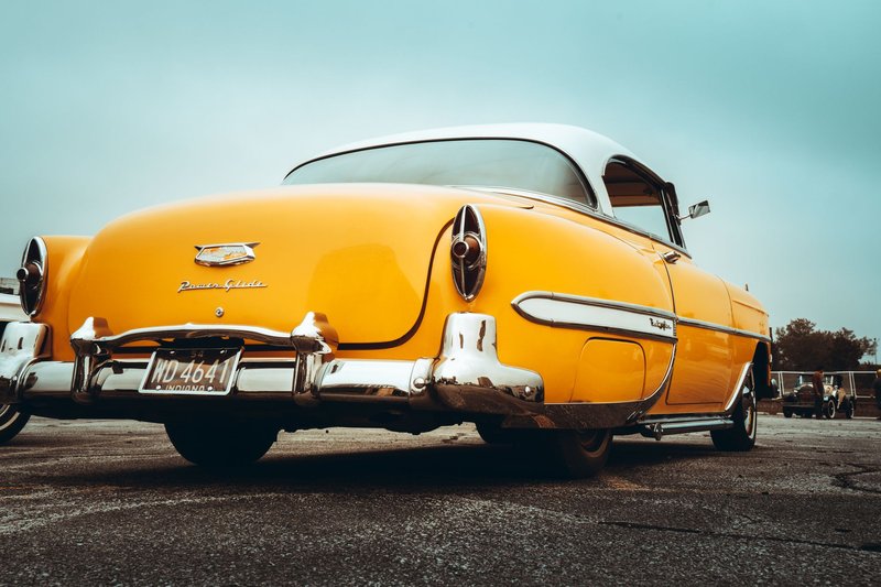 Low angle view of a vintage yellow classic American car in an outdoor setting.