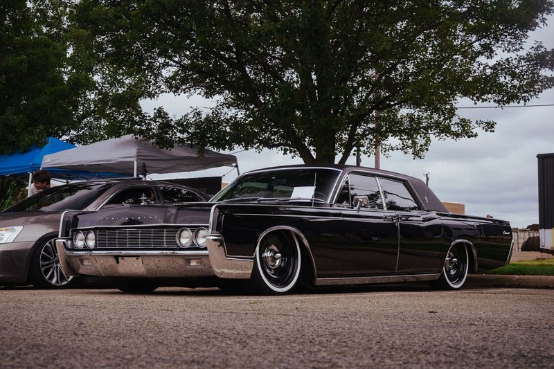 Vintage Lincoln Continental showcased in an outdoor car exhibition, under trees.