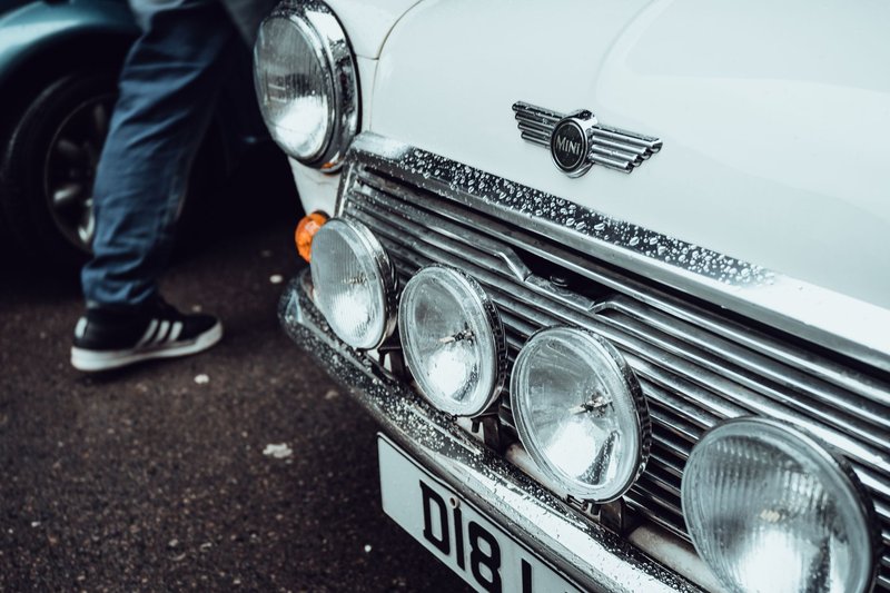 Close-up of a classic Mini Cooper showing the front with headlights and raindrops on the hood.