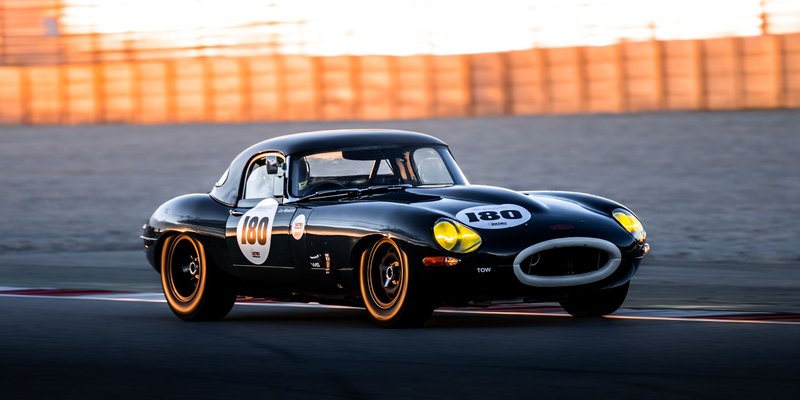 Vintage race car speeding on track during sunset, showcasing classic design and speed.