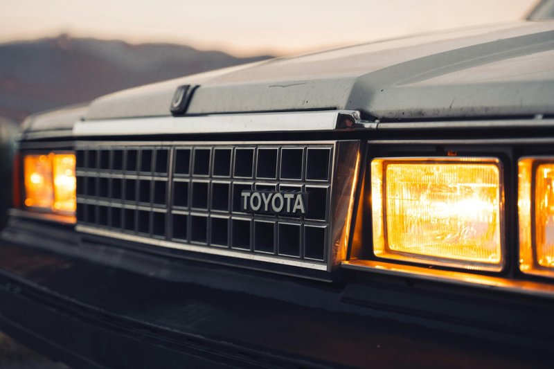 Close-up of classic Toyota Cressida featuring its iconic grille and glowing headlights at sunset.