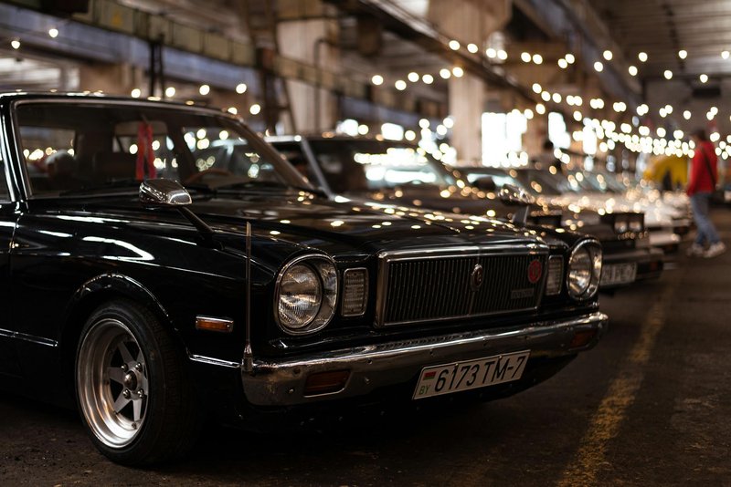 A vintage black Toyota on display at an indoor car show with bokeh lights.
