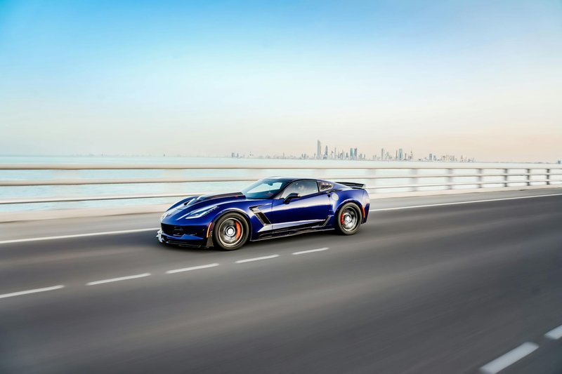 Dynamic shot of a blue Corvette cruising on a highway in Kuwait with the city skyline in the background.