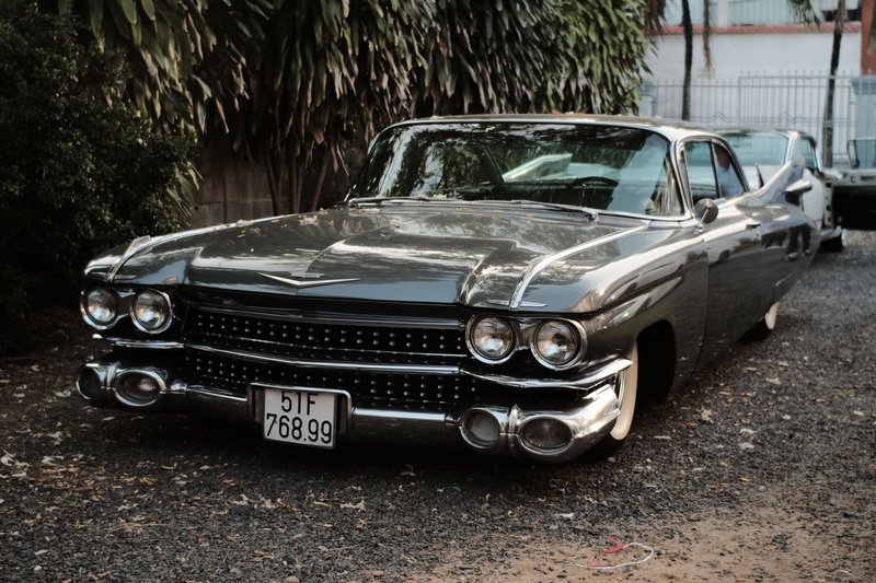 Vintage black Cadillac coupe de ville parked on gravel against a leafy backdrop.