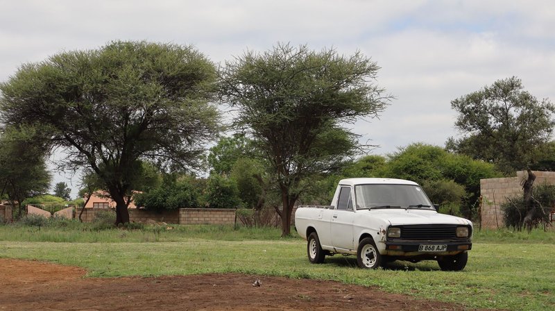A vintage white pickup truck parked in a rural landscape among lush greenery under a cloudy sky.