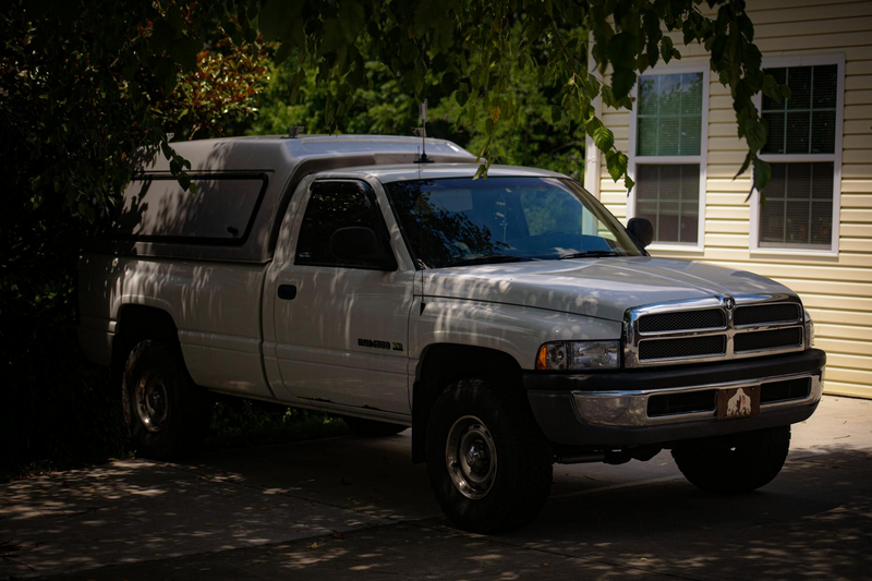 A white Dodge Ram pickup truck parked in a shaded driveway beside a house.
