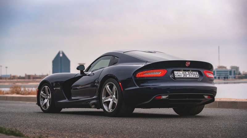 A sleek black Dodge Viper sports car parked on a city road with skyline.