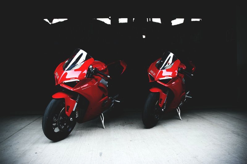 Two striking red Ducati sports bikes parked in a shadowy garage setting.