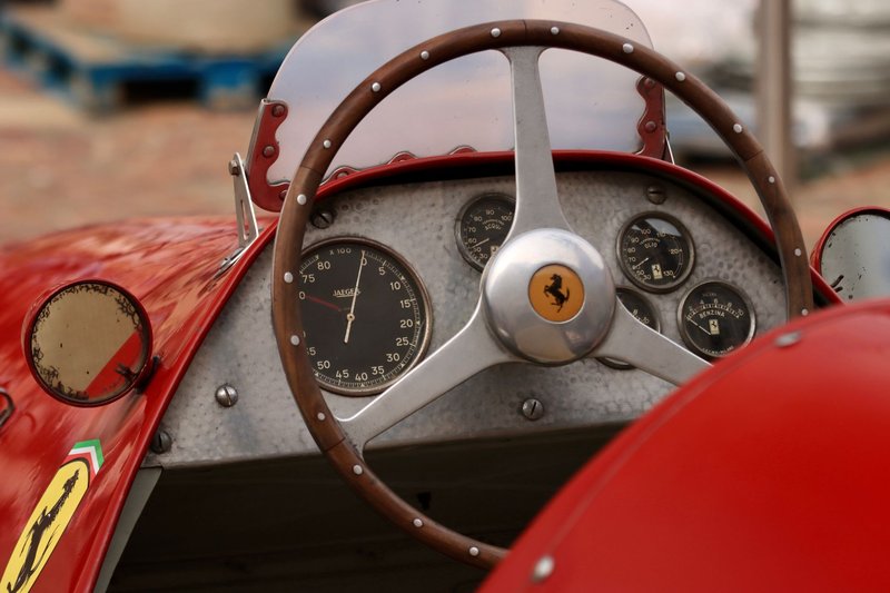 Close-up of a vintage race car cockpit featuring a Ferrari emblem on the steering wheel with classic dials.