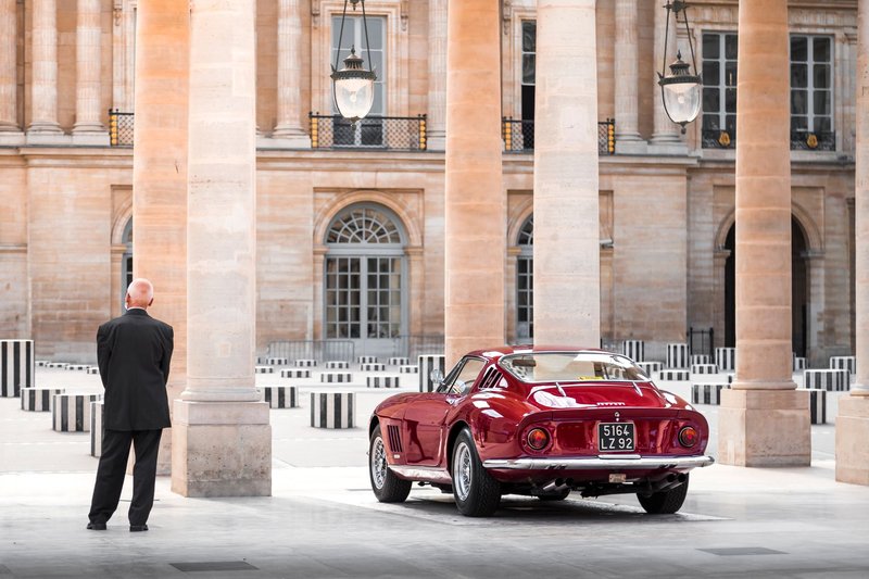 A vintage red sports car parked in a historic European architectural setting.