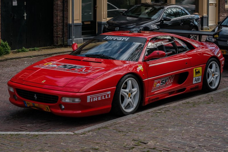 A vibrant red Ferrari sports car parked on a European street, showcasing racing stickers and classic design.