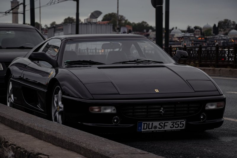 Black Ferrari F355 supercar parked on bustling Istanbul street, showcasing urban luxury and elegance.