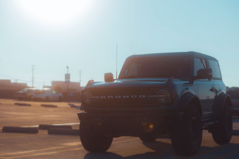 Sunlit view of an SUV in an empty parking lot, featuring a Ford Bronco.