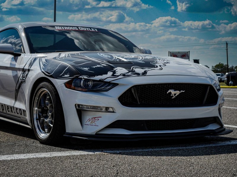 Close-up of a white Ford Mustang with custom decals in Ennis, TX parking lot.