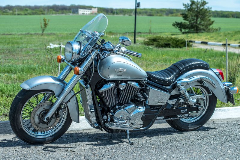 A chrome motorcycle parked on a quiet countryside road with lush green fields in the background.