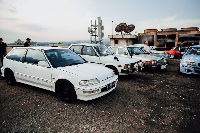 A collection of classic cars and enthusiasts gathered on a rooftop for a photo shoot.