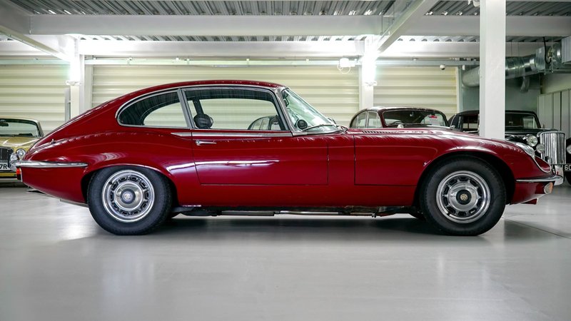 Side view of a vintage red Jaguar E-Type classic car parked indoors in a garage.