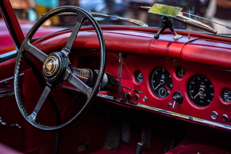 Close-up view of a vintage Jaguar XK150 red car interior showcasing the steering wheel and dashboard.