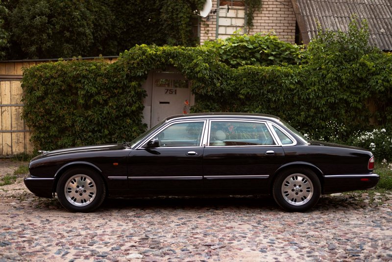 Elegant black Jaguar XJ parked on a cobblestone street with lush greenery backdrop.