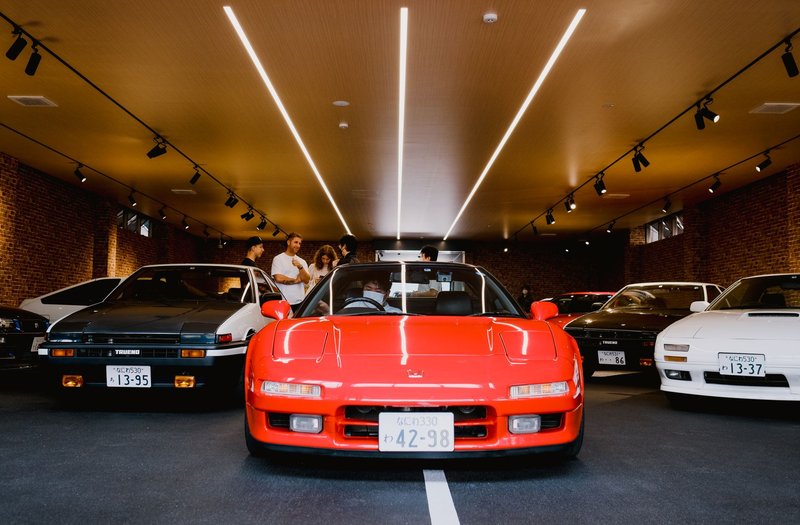 A selection of vintage Japanese cars displayed at an indoor car exhibition with people admiring them.