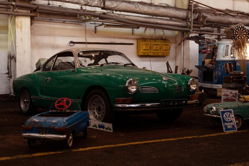 A green vintage Volkswagen Karmann Ghia displayed at an indoor classic car exhibition.