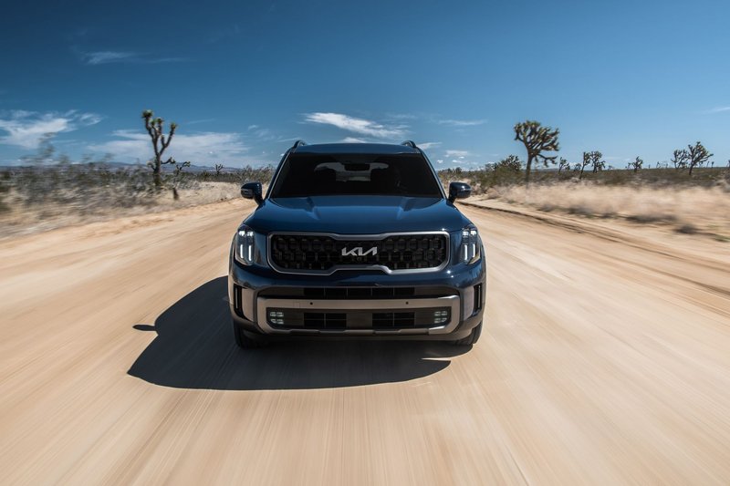 Front view of an SUV driving fast on a desert dirt road under a clear blue sky.